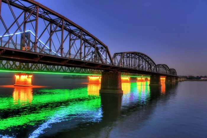 Hady Khandani, HDR - ILLUMINATED SINO-KOREAN FRIENDSHIP BRIDGE OVER YALU RIVER BETWEEN CHINA AND NORTH KOREA - DANDONG 06 (Yalu, Fluss, Brücke, Freundschaftsbrücke, Bauwerk, Konstruktion, Beleuchtung, Spiegelungen, neonfarben, Dämmerung, Dandong, China, Nordkorea, Fotokunst, Wohnzimmer, Treppenhaus,  Wunschgröße, bunt)