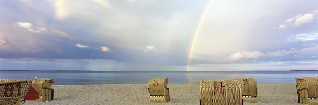 Heinrich Hecht, Sunshine And Rain (Strand, Meer, Strandkörbe, Sommer, Sandstrand, Urlaub, Regenbogen, maritim, Meeresbrise, Badezimmer, Treppenhaus, Wohnzimmer, Fotokunst, bunt)