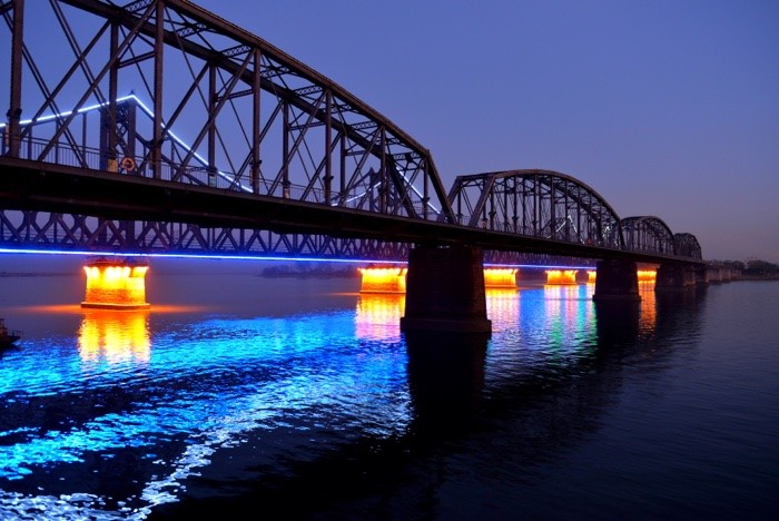 Hady Khandani, ILLUMINATED SINO-KOREAN FRIENDSHIP BRIDGE OVER YALU RIVER BETWEEN CHINA AND NORTH KOREA - DANDONG - BLUE (Yalu, Fluss, Brücke, Freundschaftsbrücke, Bauwerk, Konstruktion, Beleuchtung, Spiegelungen, neonfarben, Dämmerung, Dandong, China, Nordkorea, Fotokunst, Wohnzimmer, Treppenhaus,  Wunschgröße, bunt)