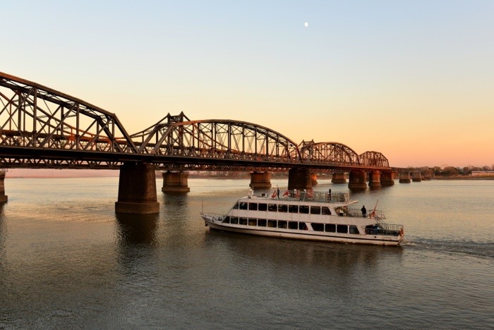 Hady Khandani, SINO-KOREAN FRIENDSHIP BRIDGE OVER YALU RIVER BETWEEN CHINA AND NORTH KOREA - DANDONG 1 (Yalu, Fluss, Brücke, Ausflugsboot, Boot, Freundschaftsbrücke, Bauwerk, Konstruktion, Dandong, China, Nordkorea, Fotokunst, Wohnzimmer, Treppenhaus,  Wunschgröße, bunt)