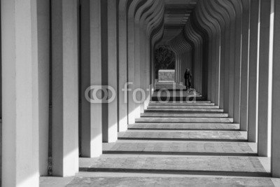 nikhg, Ragazza che cammina in un corridoio porticato (vorhalle, mädchen, weiblich, korridor, vorhalle, bergpass, schwarzweiß, tunnel, schwarz, weiß, architektur, licht, licht, kurve, verbiegen, gekrümmt, kolonne, kolonne, spazieren, spaziergang, gebäude, modern, modern, beton, beton, reihe, linie, bedeck)