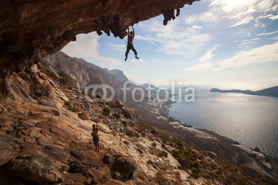 Andrey Bandurenko, Rock climber climbing at the rock , Kalymnos Island, Greece (bergsteiger, klettern, klettern, fels, sichern, felsen, paar, griechenland, höhe, hoch, leute, seil, szenerie, meer, anblick, jung, frau, aktiv, betätigung, wölben, cave, herausforderung, schwer, abend, extrem, guy, holding, insel, landschaft, ble)