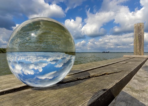 Rolf Fischer, Kugelwelt am Steg (Bootssteg, Glaskugel, Kugel, Himmel, Wolken, Spiegelung, verkehrte Welt, auf dem Kopf stehen,  Holzbohlen, Holzsteg, Badezimmer, Arztpraxis, Wohnzimmer, Wunschgröße,  bunt)