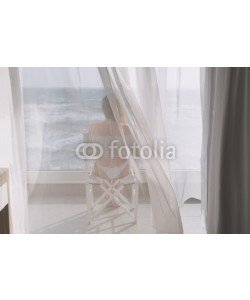 flowertiare, Naked beautiful female in the lace bikini sitting on the chair behind the transparent curtain on the glass balcony against the backdrop of the sea