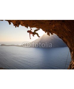 Andrey Bandurenko, Rock climber climbing along roof in cave at sunset