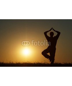am, Silhouette of a man in a position Vrikshasana at exercising yoga on a grassy horizon at sunset.